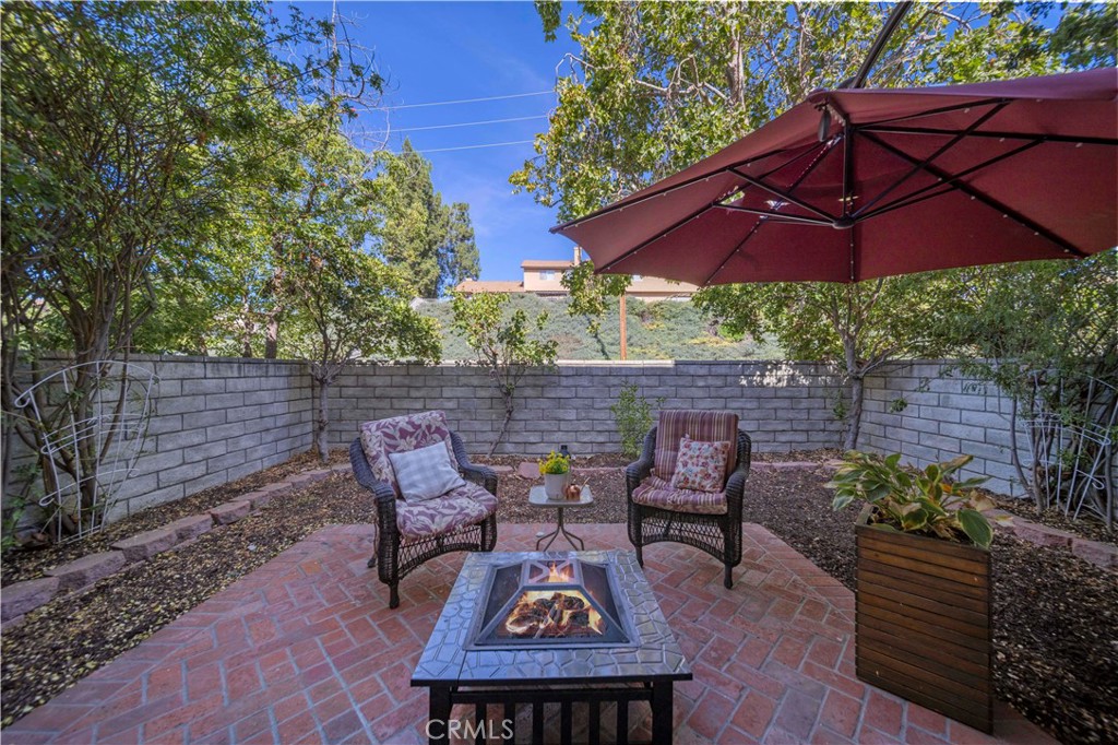 Backyard patio with a square fire pit, two cushioned chairs, and a burgundy umbrella.