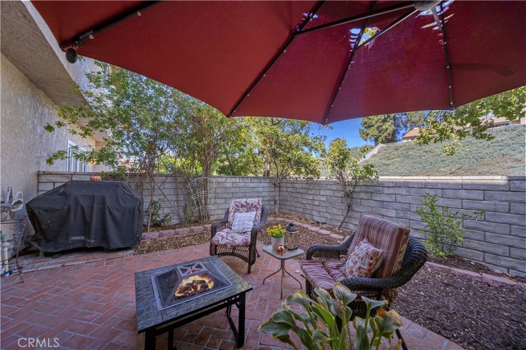 Brick patio with wicker seating, a fire pit table, covered grill, and large red umbrella.