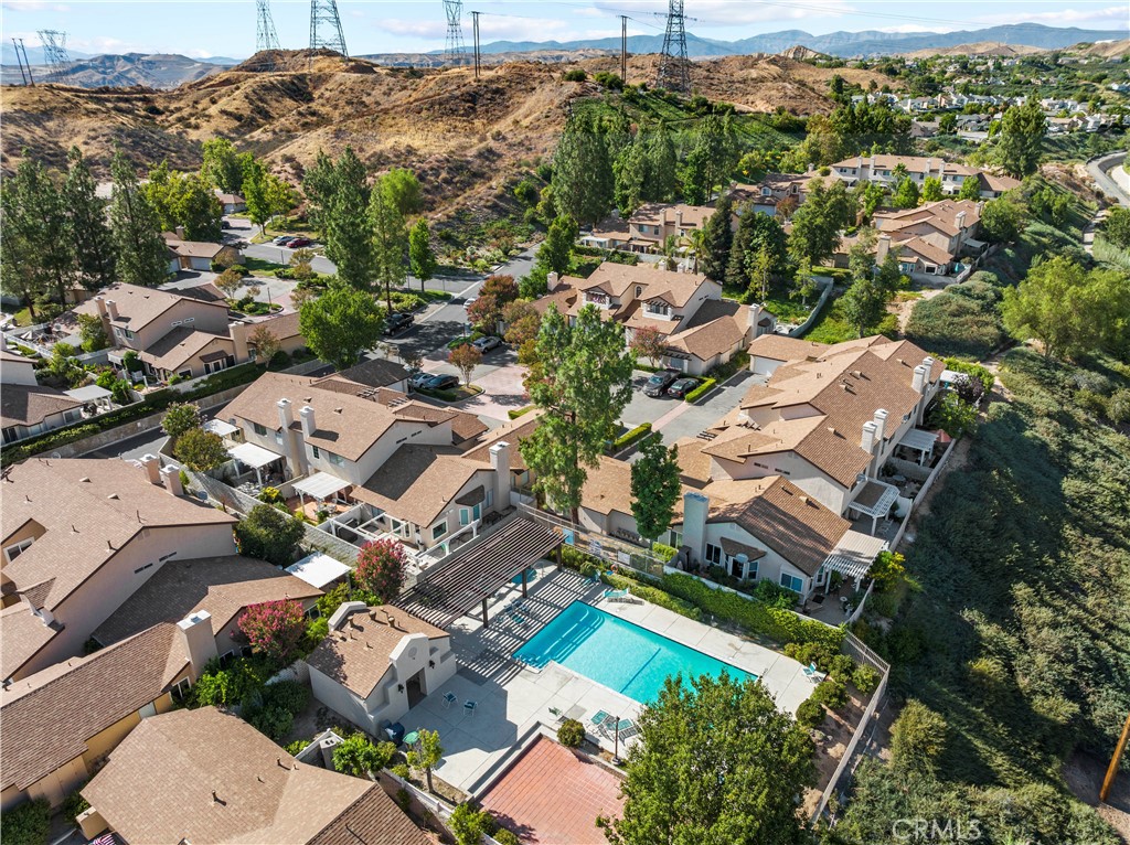 Aerial view of tan-roofed townhomes surrounding a community pool, with dry hills and mountains beyond.