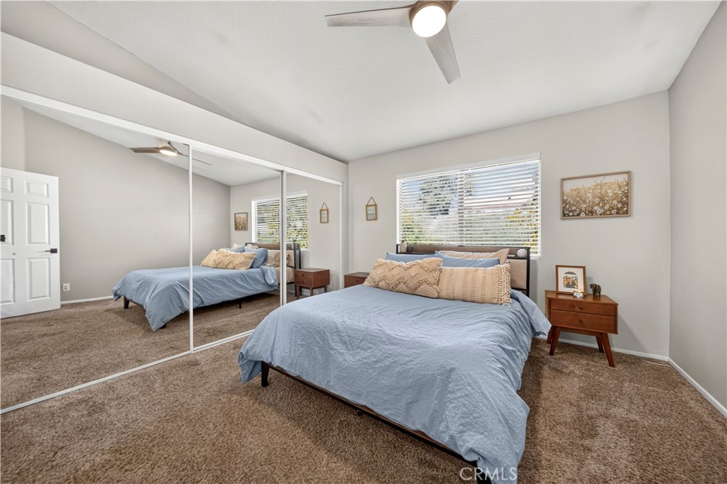 Bedroom with a blue-covered bed, mirrored closet doors, beige carpet, and a ceiling fan.