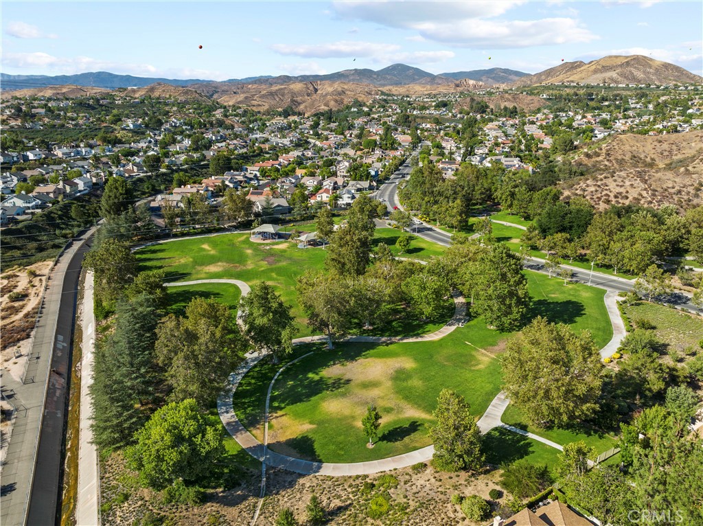 Aerial view of a neighborhood park with curving paths, trees, homes, and distant mountains.
