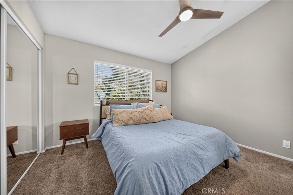 Bedroom with a light blue bedspread, wooden nightstand, mirrored closet doors, and ceiling fan.