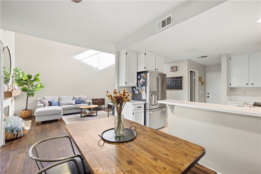 Open-plan kitchen and living area with stainless-steel appliances, white cabinets, and a wood dining table.