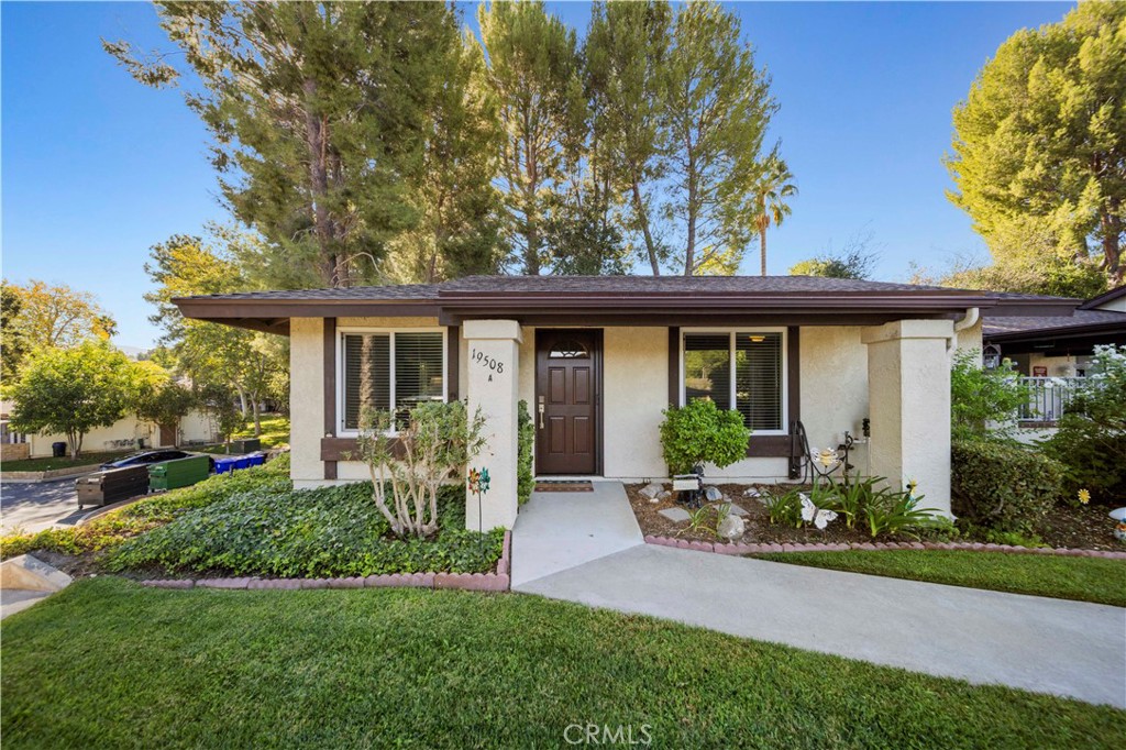 Single-story stucco house with a dark brown front door, landscaped garden beds, and a broad lawn.