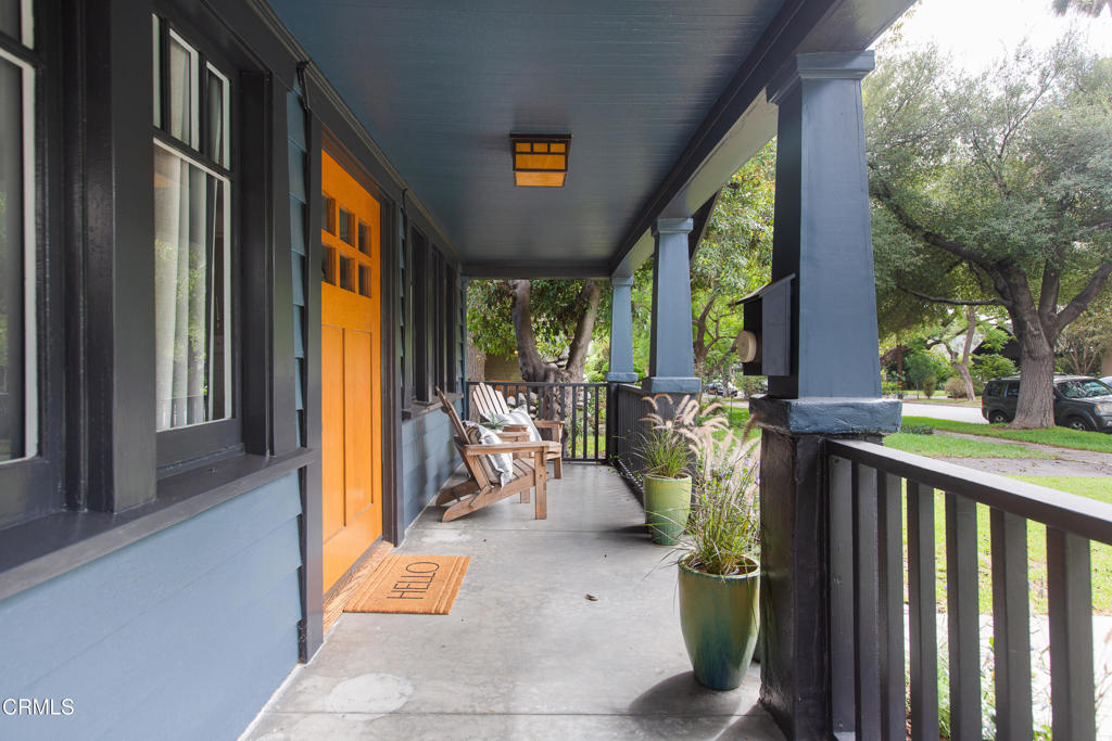 Covered front porch with an orange entry door, rocking chairs, and potted plants.