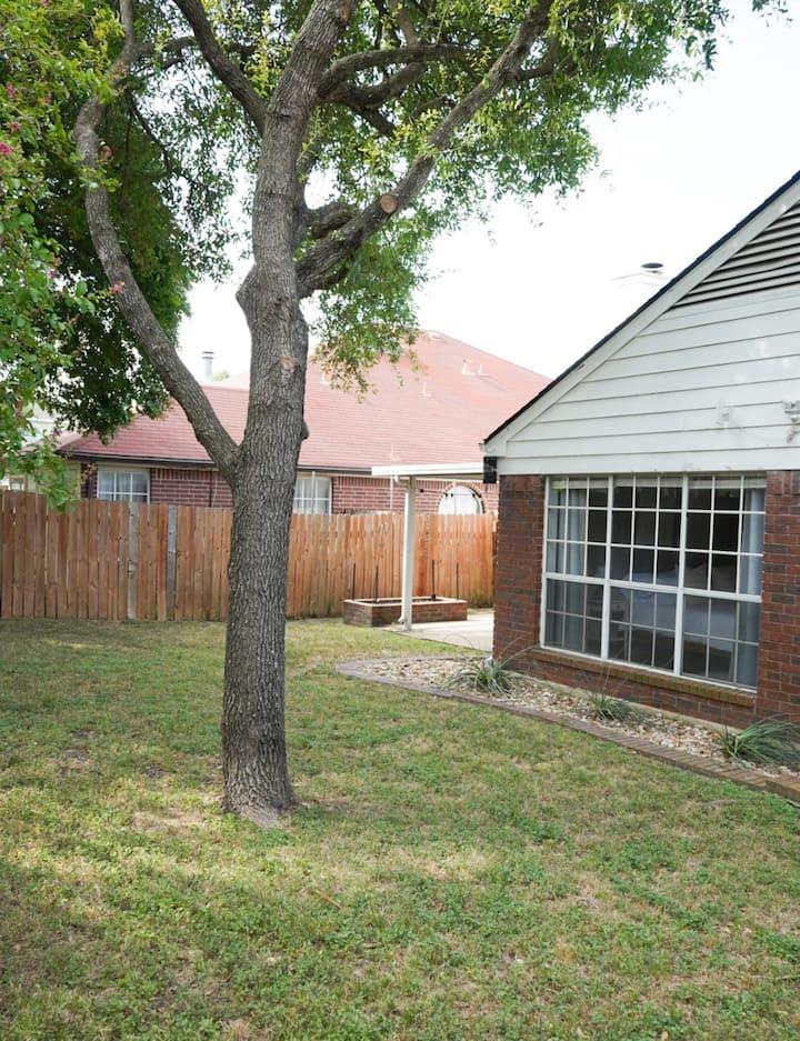 Backyard with a mature shade tree, lawn, wooden privacy fence, and small patio.
