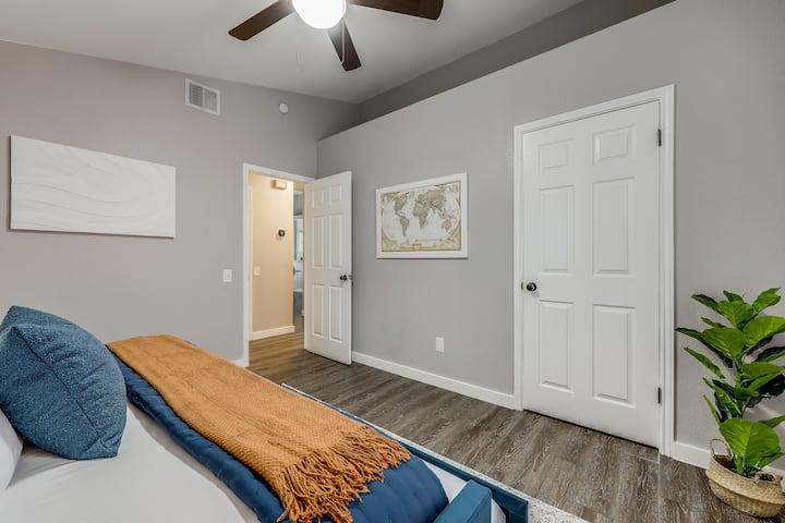 Bedroom with a blue bed, rust-colored throw, framed world map, and open door to the hallway.