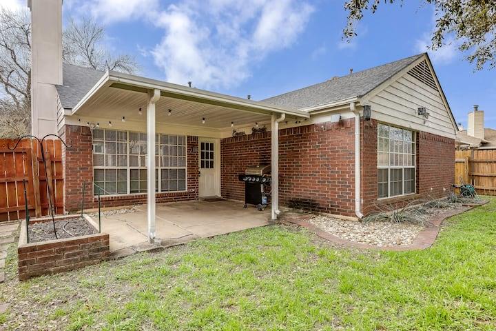 Brick home with a covered rear patio, barbecue grill, and fenced grassy yard.