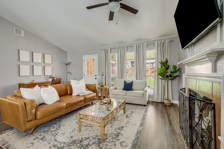 Living room with a tan leather sofa, glass coffee table, and fireplace beneath a mounted television.
