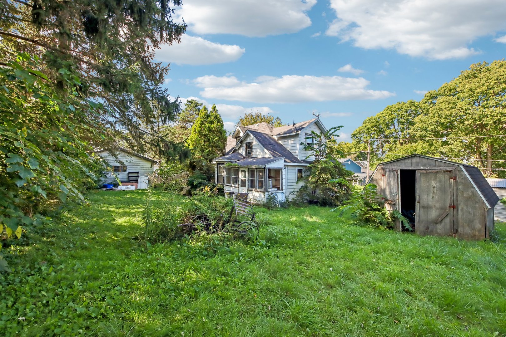 White two-story house with a screened porch and weathered shed in a leafy yard.