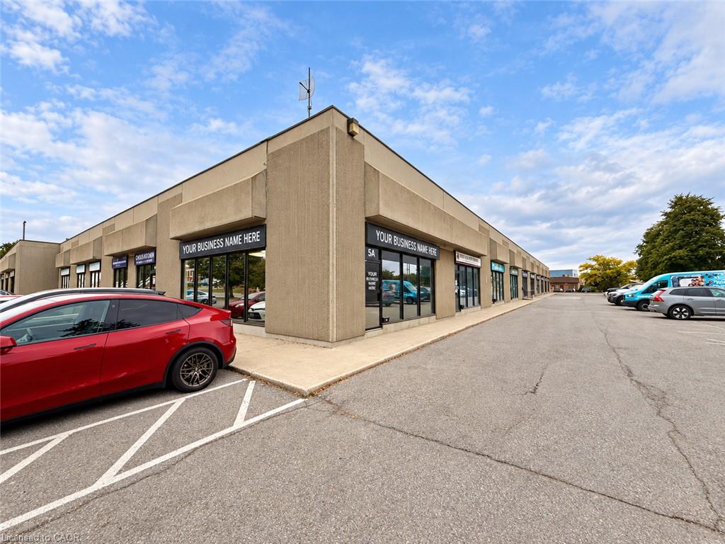 Beige commercial plaza with multiple storefronts and a red car parked in front.