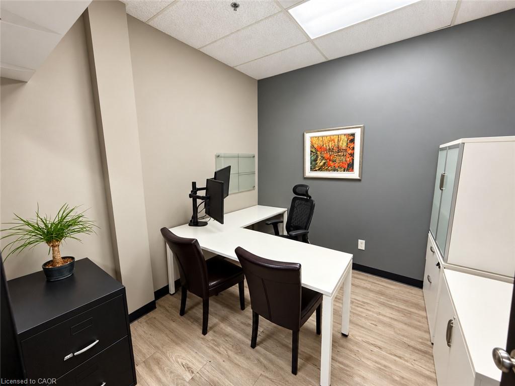 Furnished office with an L-shaped desk, computer monitors, chairs, and storage cabinets.
