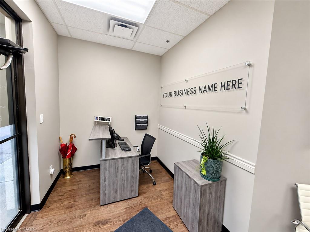 Office reception area with a gray desk, computer, potted plant, and placeholder business-name sign.