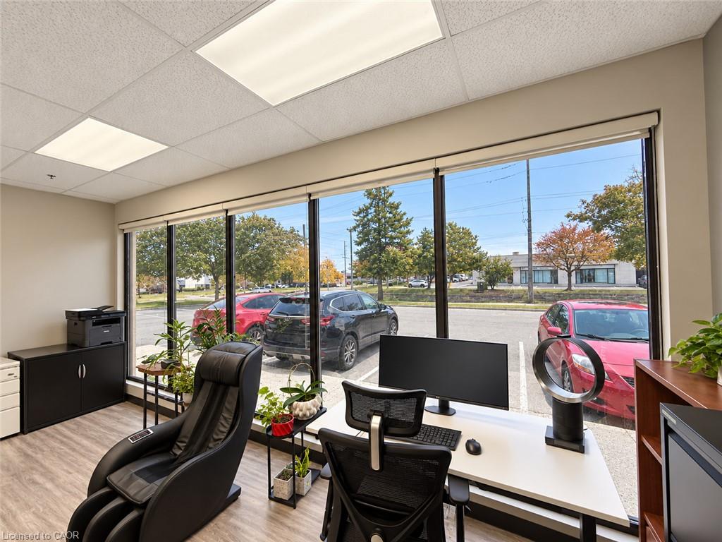 Furnished office with desks and large windows overlooking a parking lot and autumn trees.
