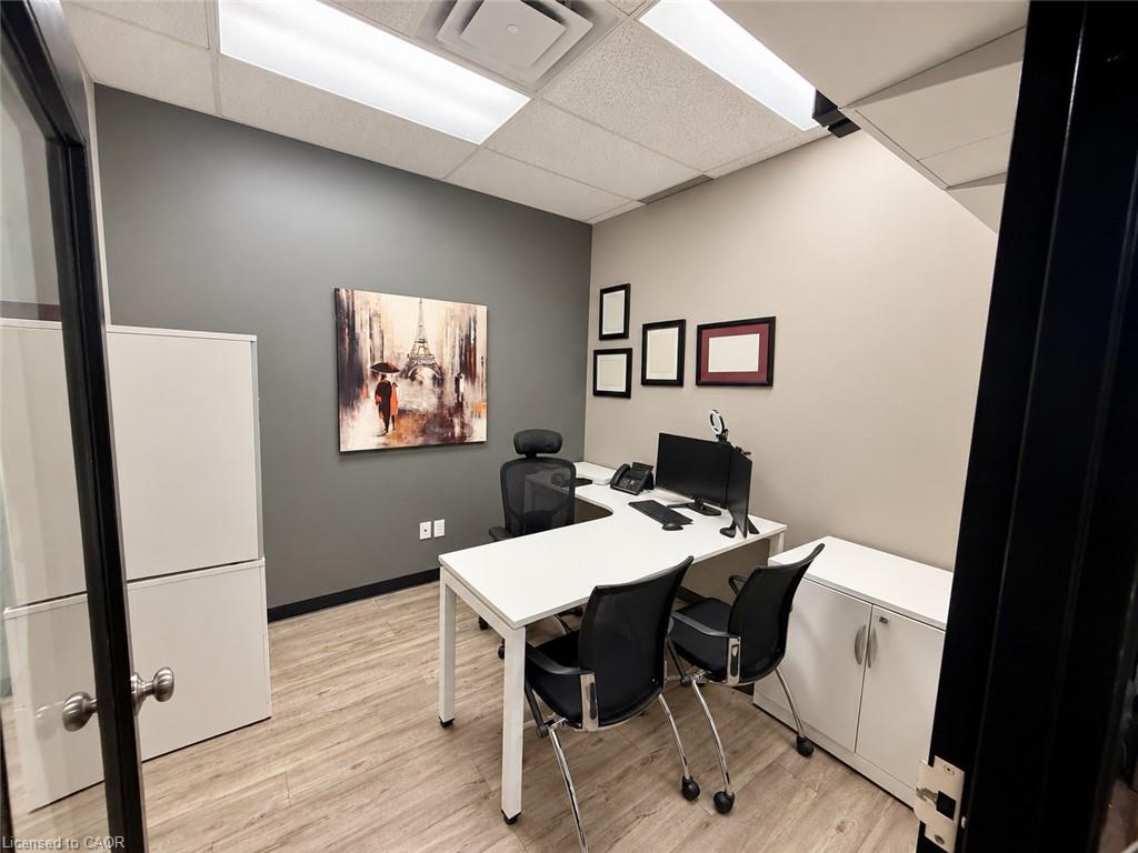 Furnished office with a white desk, black chairs, computer, and framed artwork.