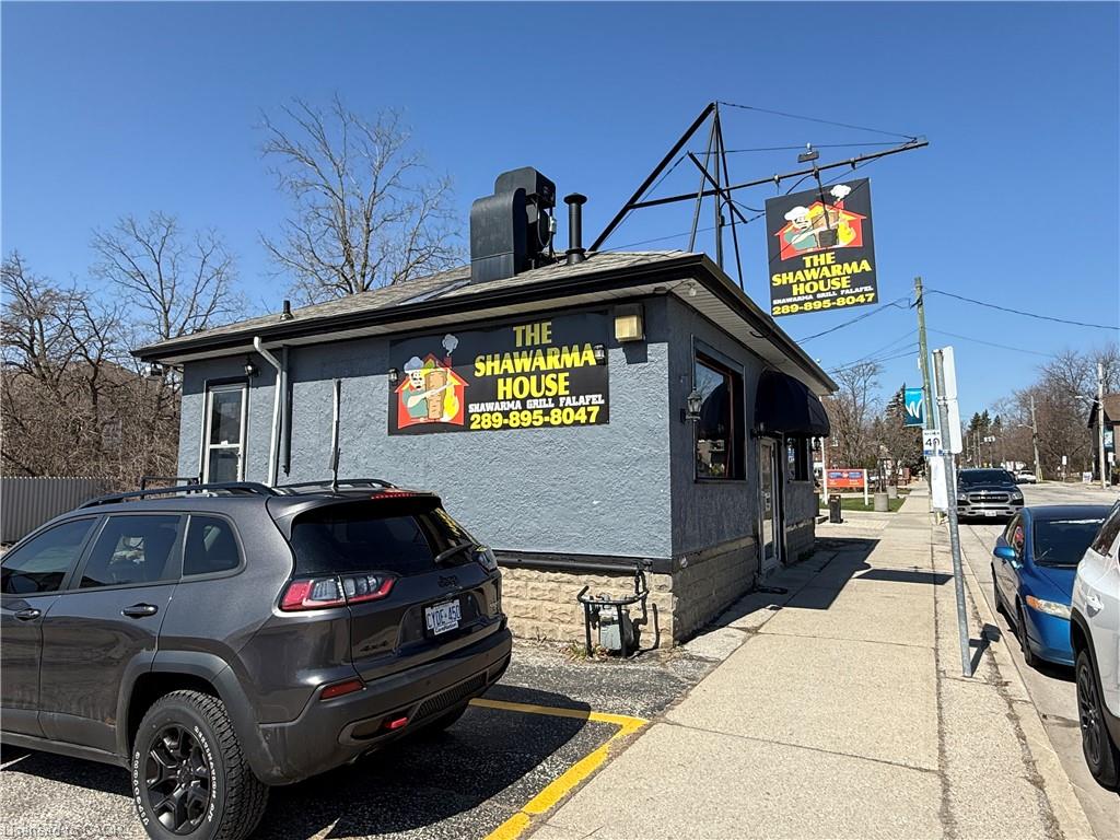 Gray Shawarma House storefront with rooftop sign beside a sidewalk and parked cars.