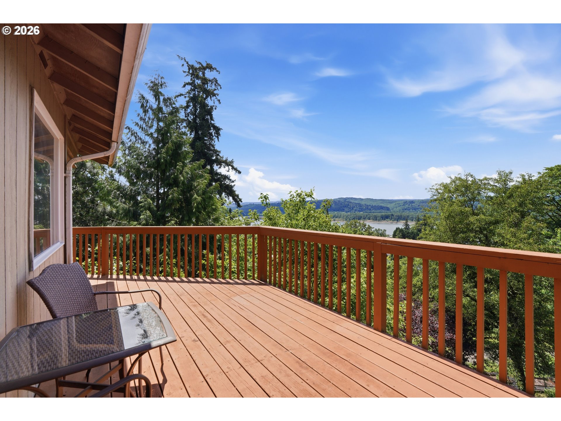 Wooden deck with outdoor seating overlooking trees, a river, and wooded hills.