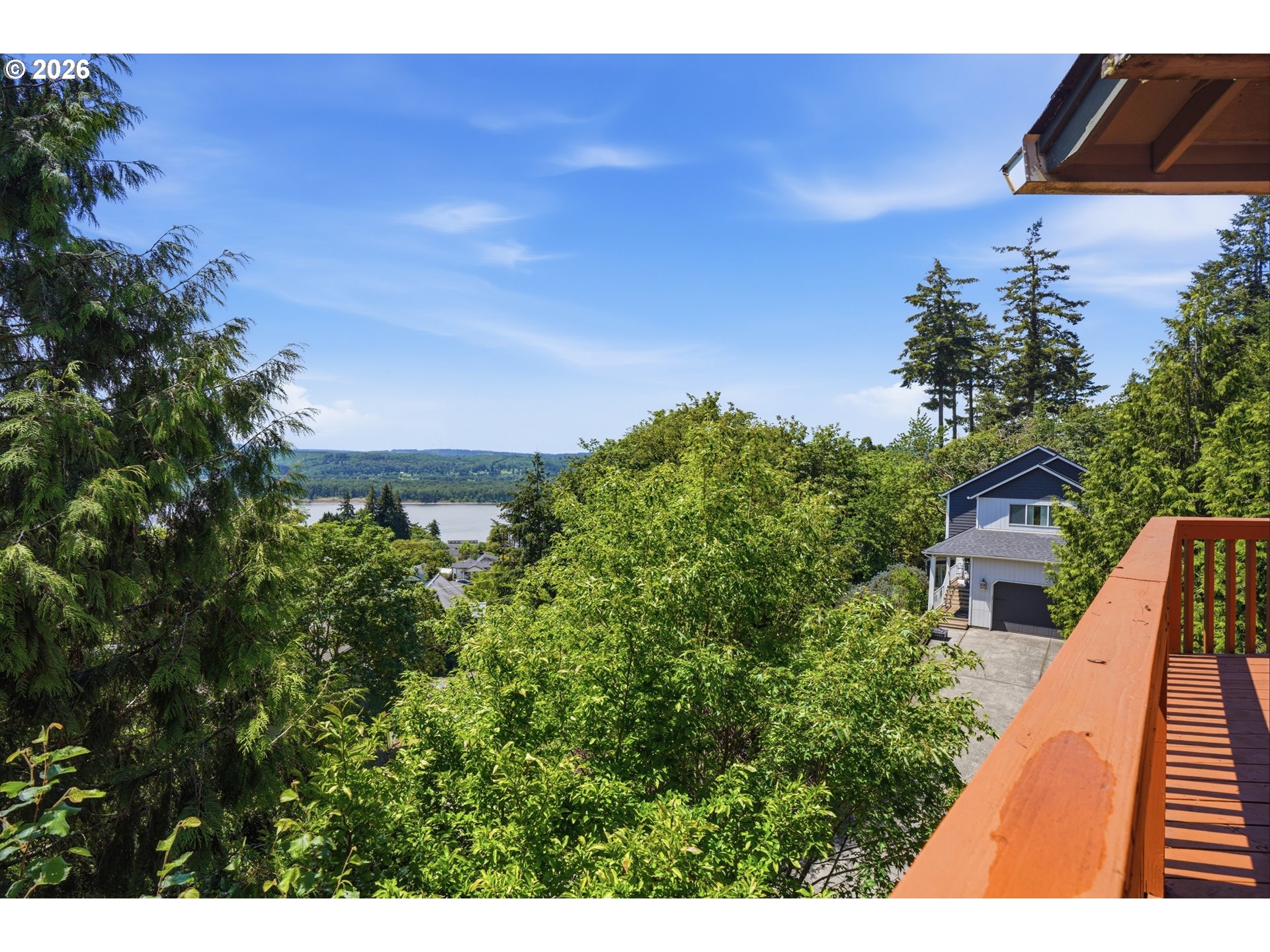 Deck view over a leafy hillside toward the water, with a neighboring house below.