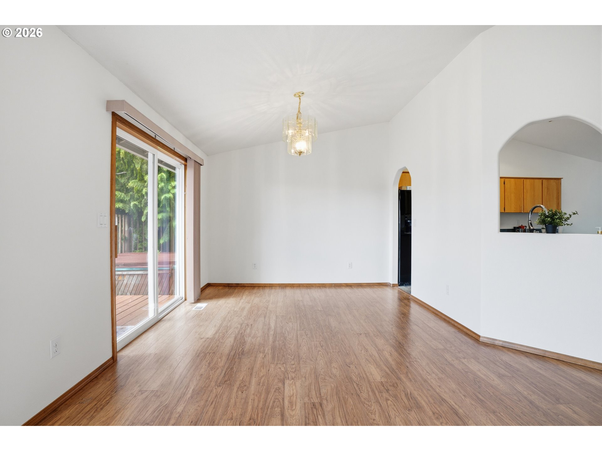 Empty dining area with wood-look floors, a chandelier, sliding glass doors, and an arched kitchen pass-through.