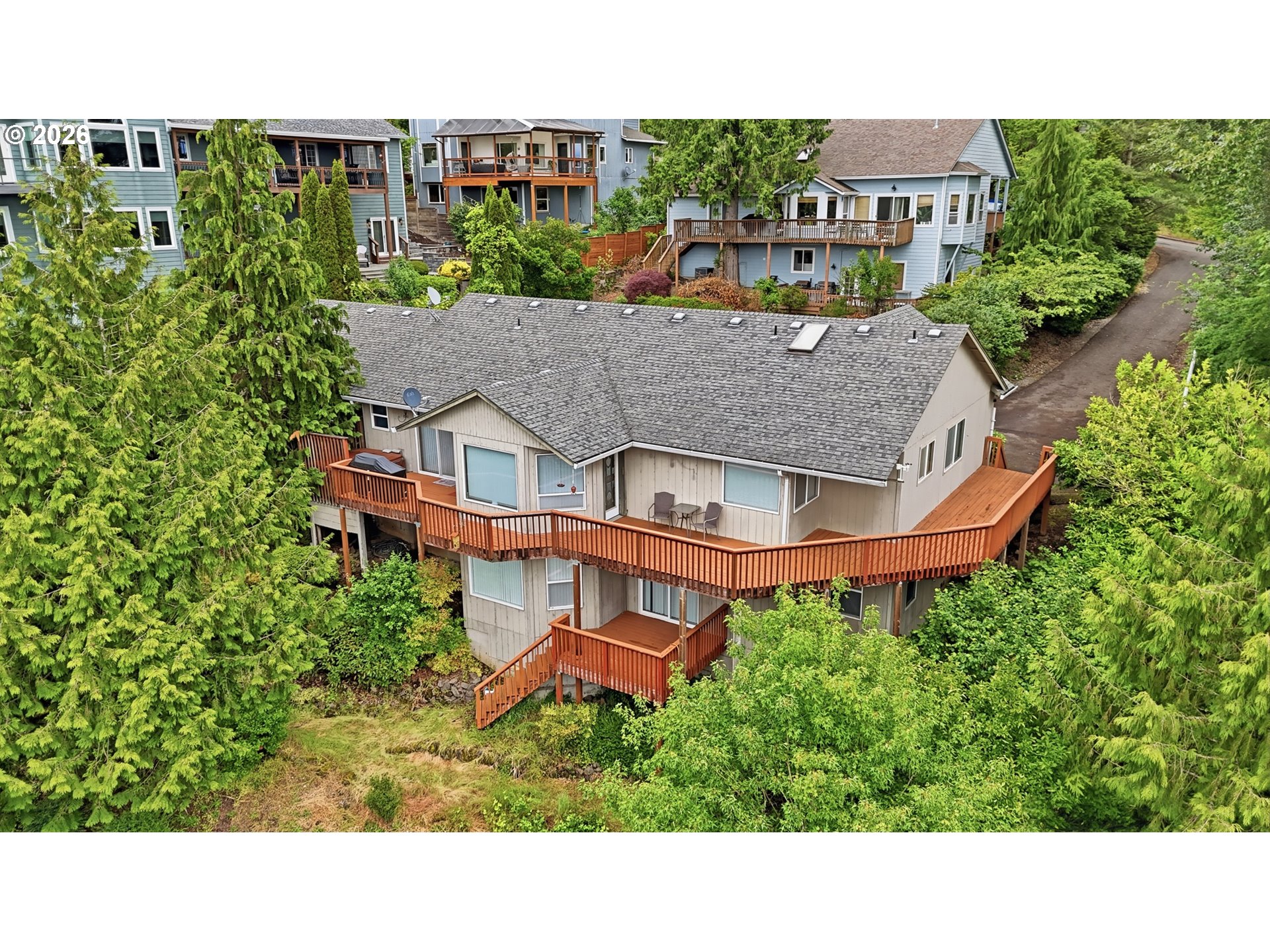 Aerial view of a two-story home with a long elevated wooden deck amid dense greenery.