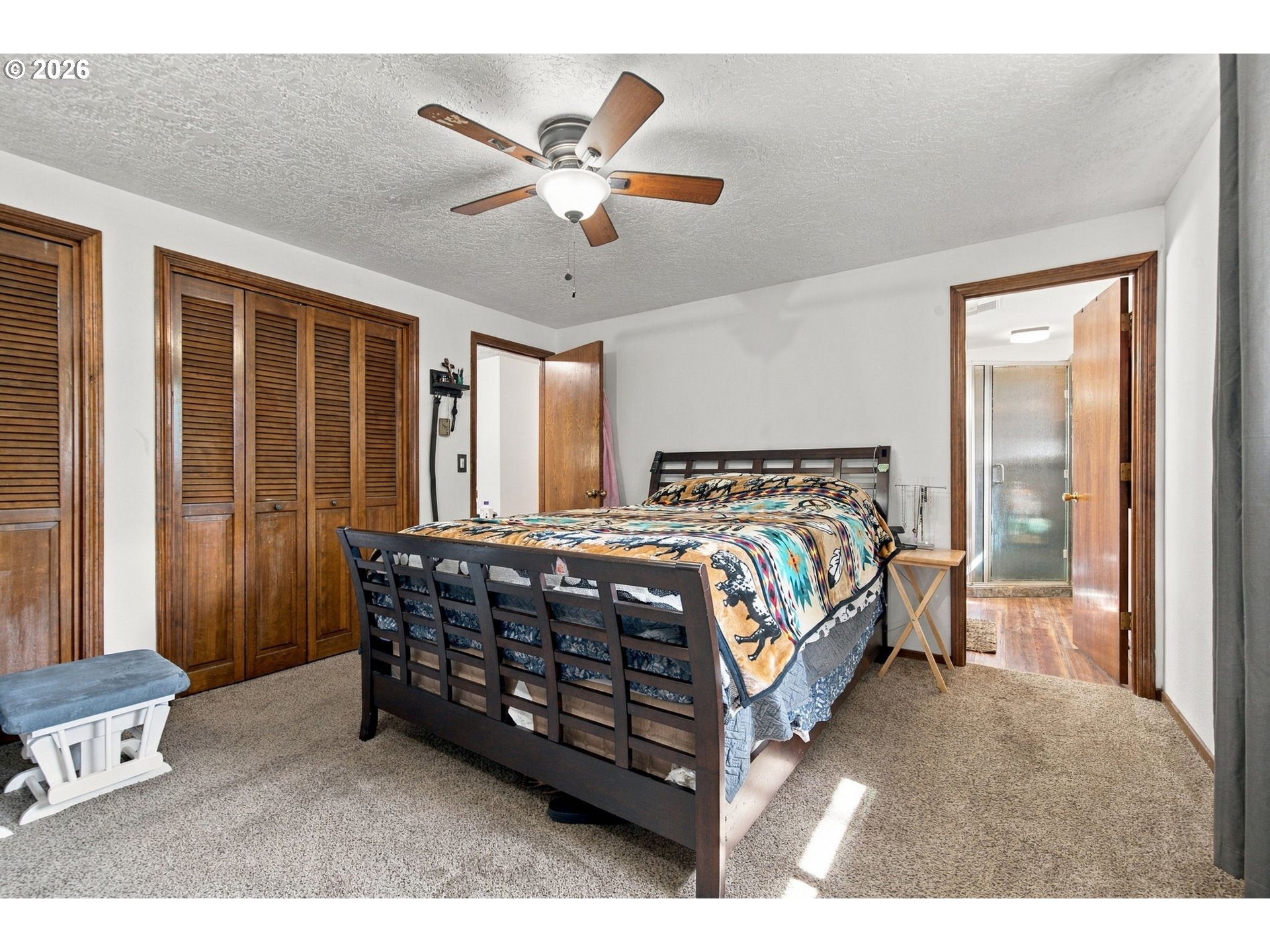 Bedroom with colorful patterned bedding, wooden closet doors, and an adjoining bathroom.