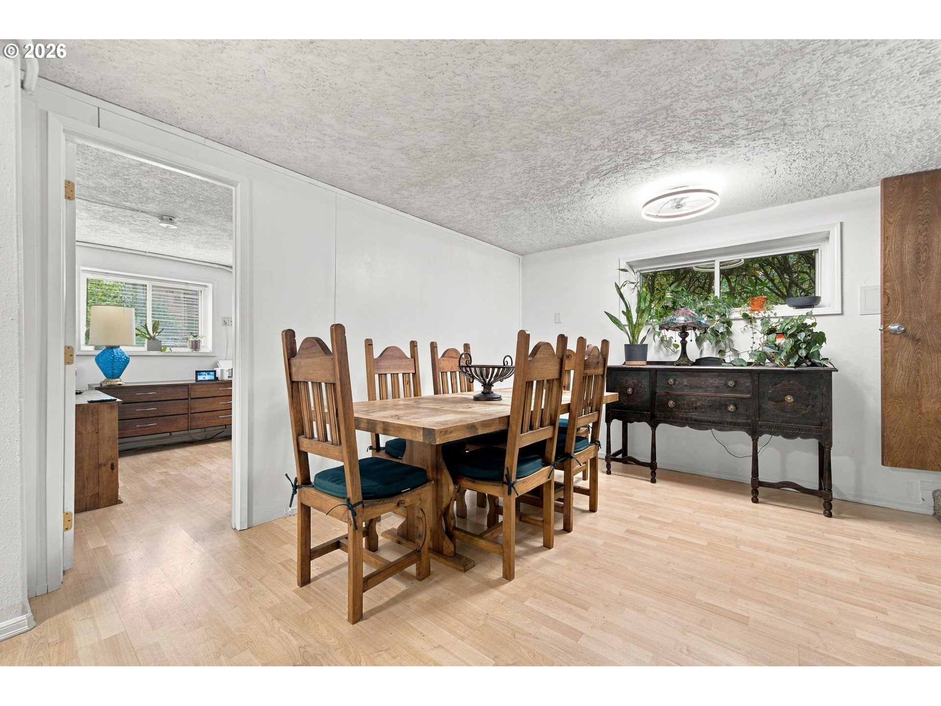 Dining room with a wooden table and chairs, antique sideboard, and plants by the window.