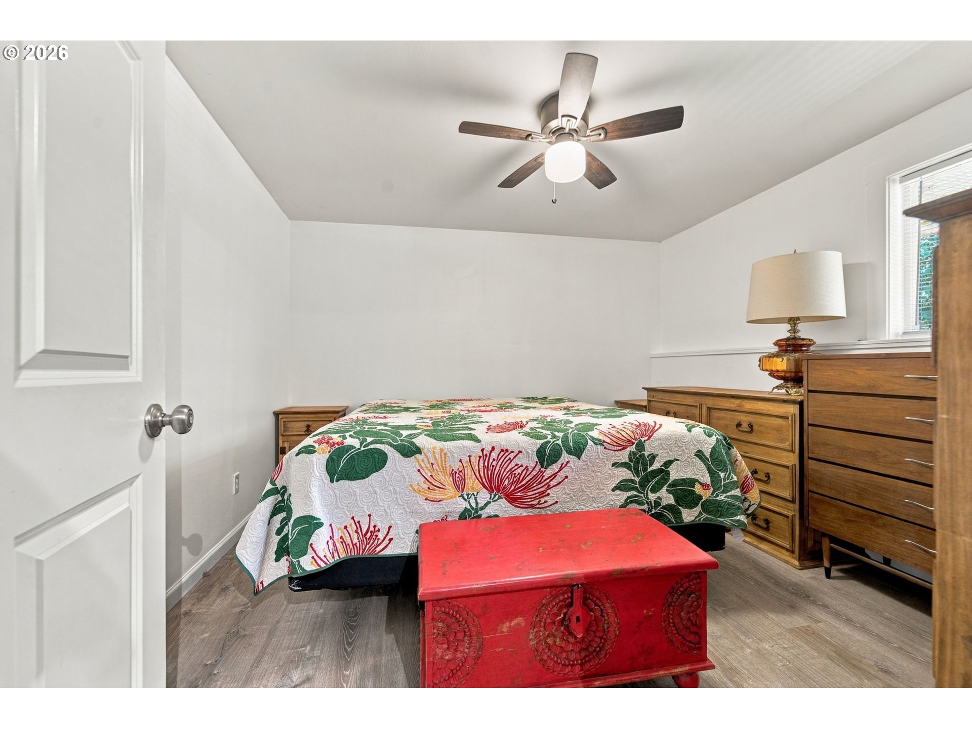 Bedroom with a floral quilt, wooden dressers, and a red carved chest at the foot of the bed.