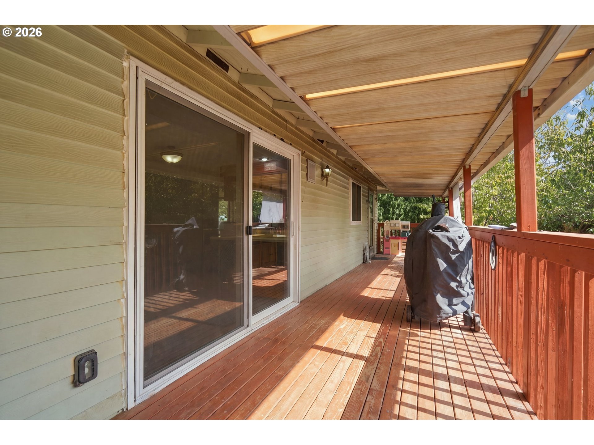 Covered wooden deck with sliding glass doors, red railing, and a covered grill.