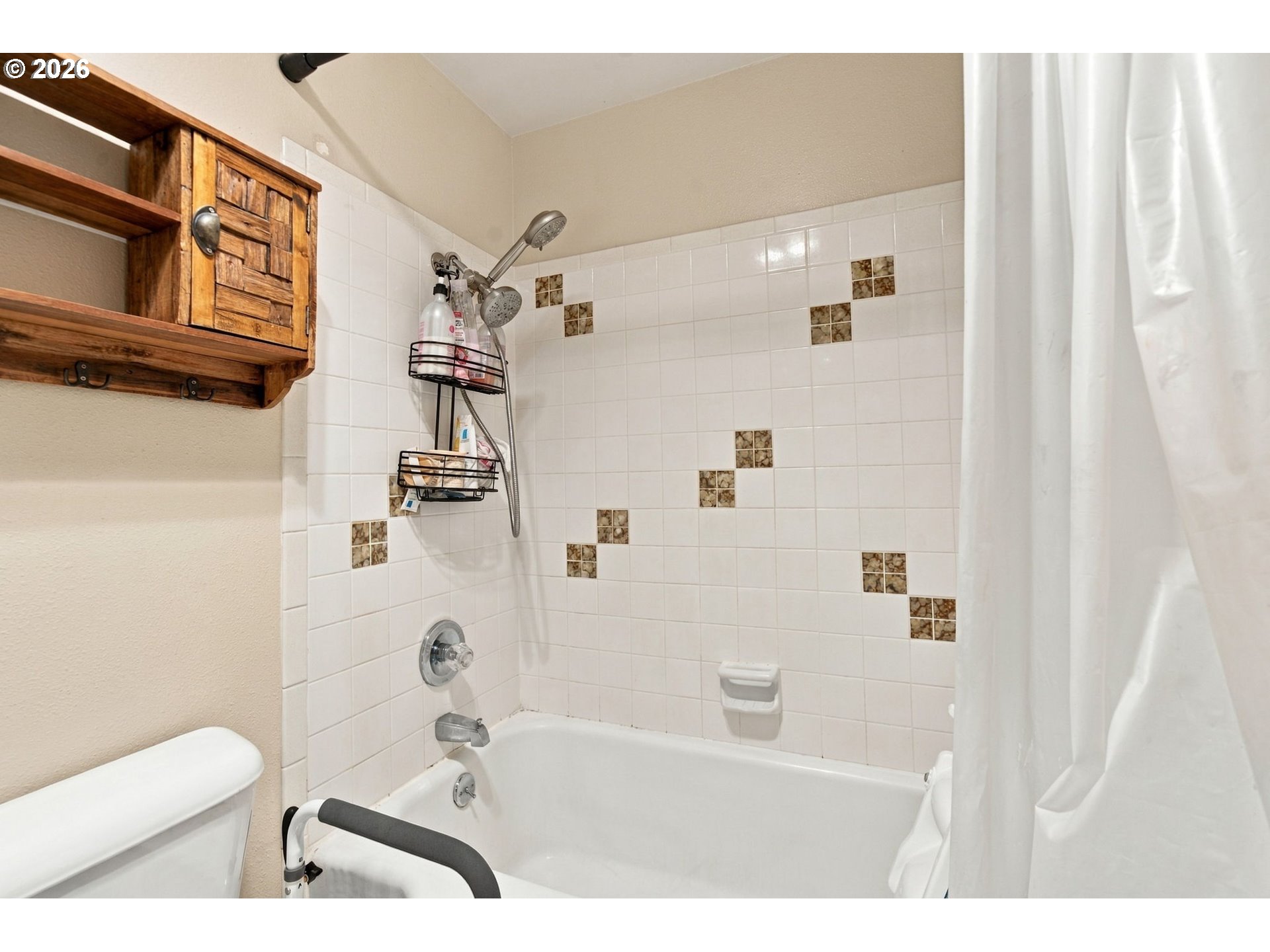 Bathroom tub and tiled shower with a wooden wall cabinet and grab bar.