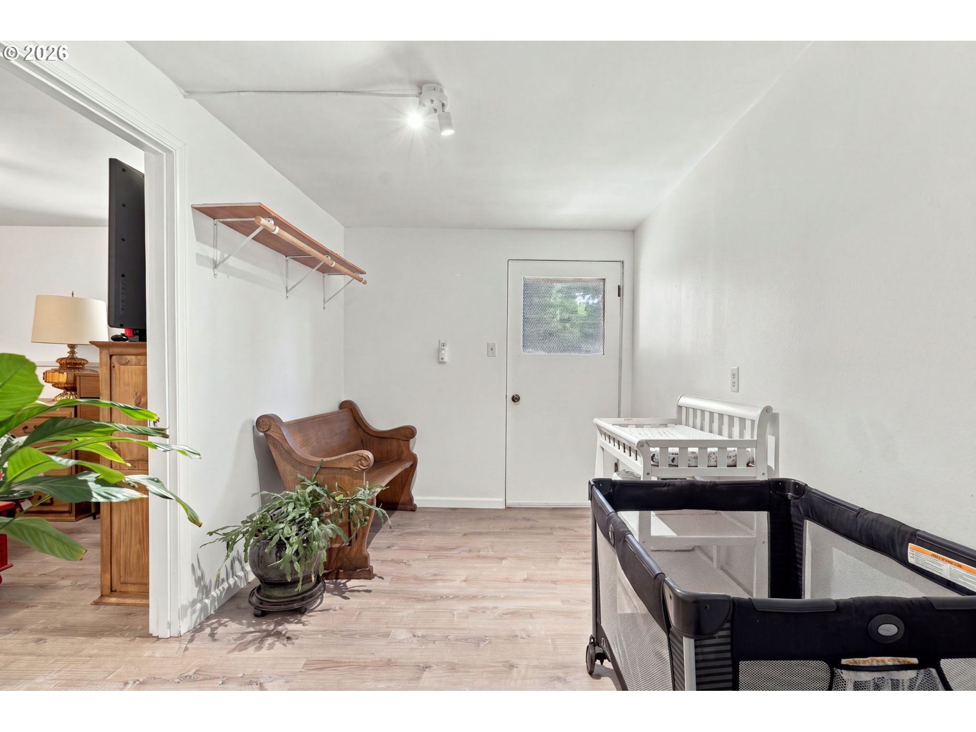 Nursery with a white crib, dark playpen, vintage wooden chair, and pale wood flooring.