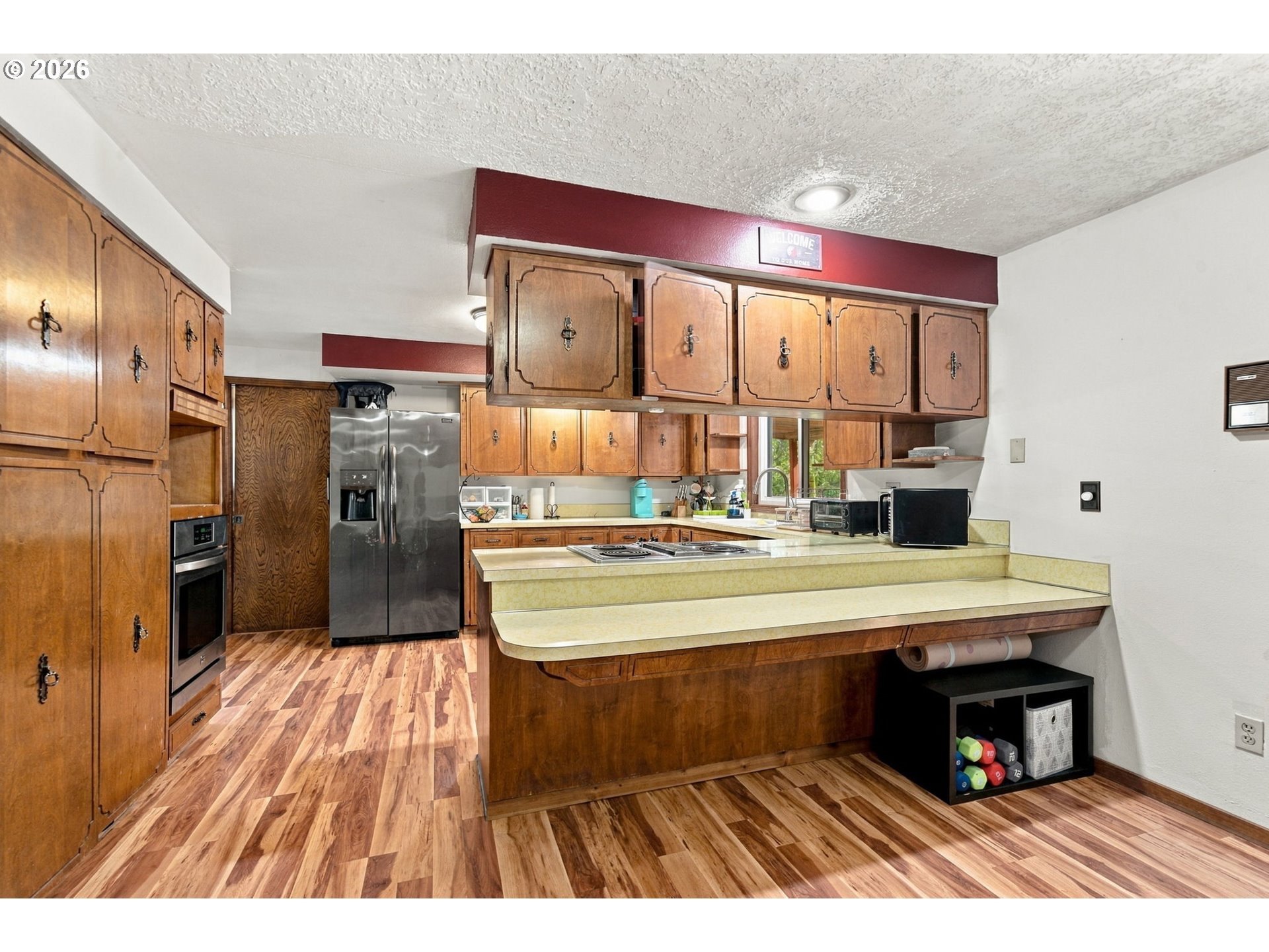Kitchen with extensive wood cabinetry, a stainless steel refrigerator, and a tiered countertop island.