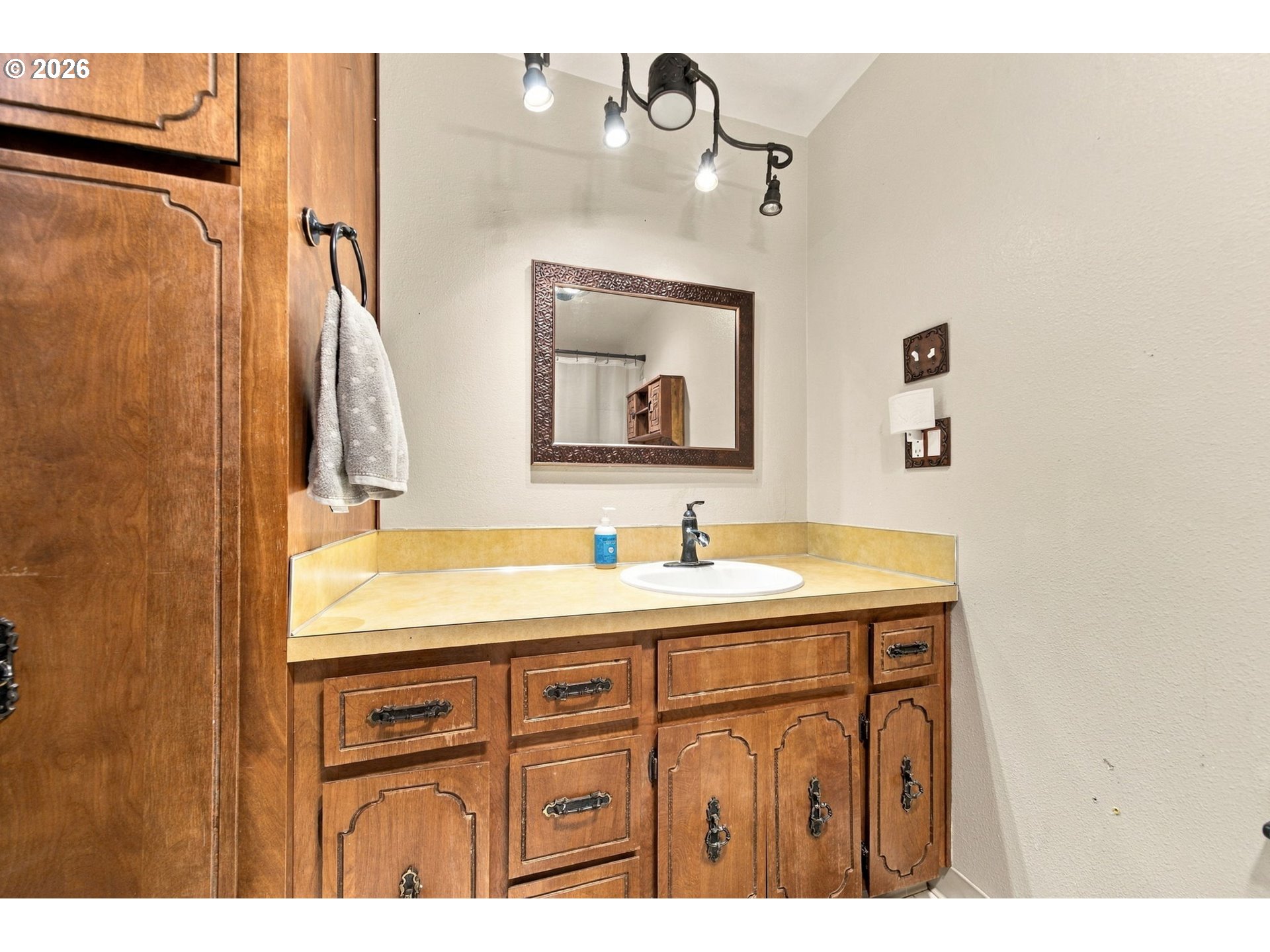 Bathroom vanity with ornate wooden cabinets, yellow countertop, oval sink, and framed mirror.