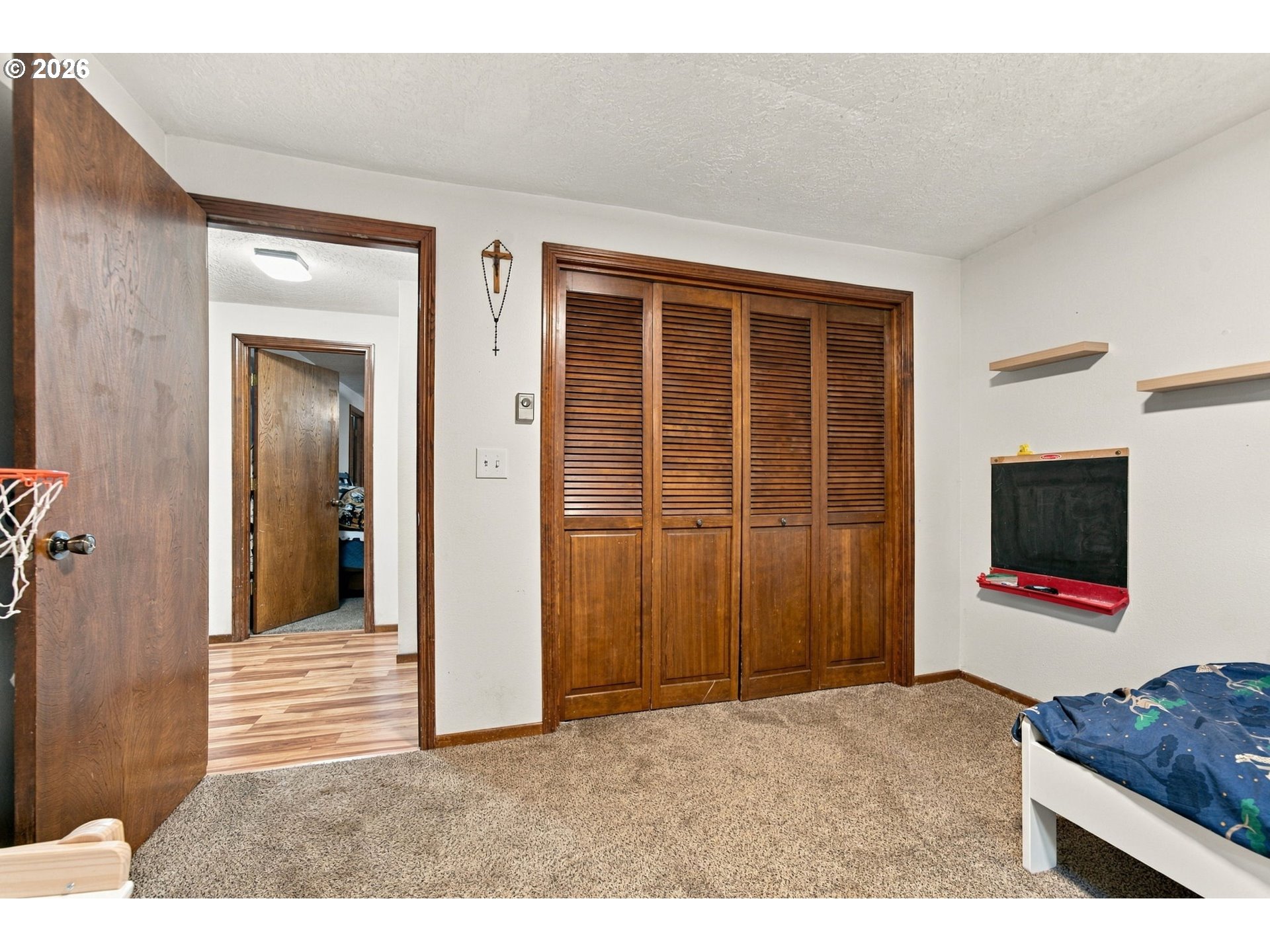 Bedroom with wooden louvered closet doors, beige carpet, and a small chalkboard.