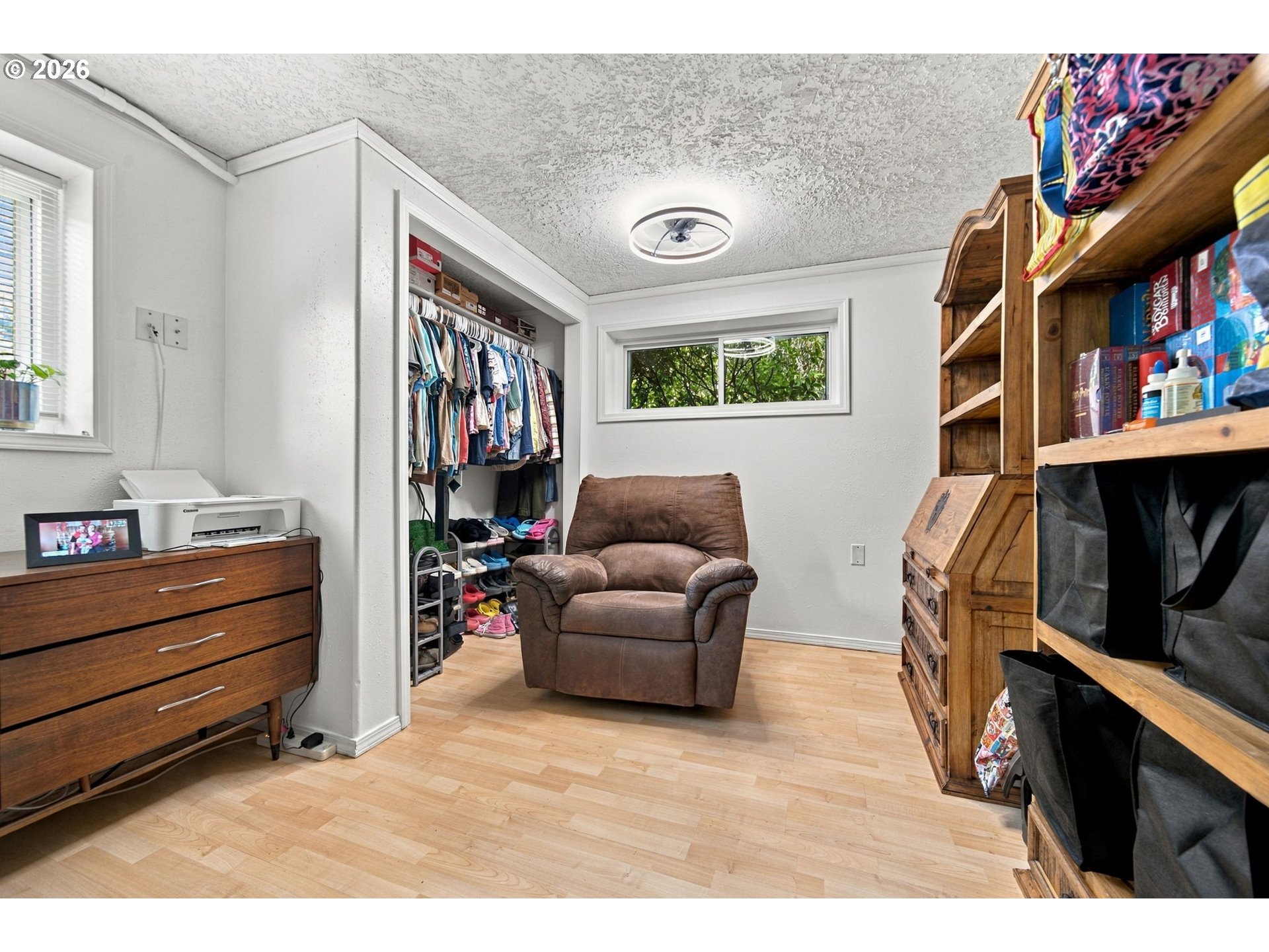 Closet and storage room with open clothing storage, wooden shelving, and a brown recliner.