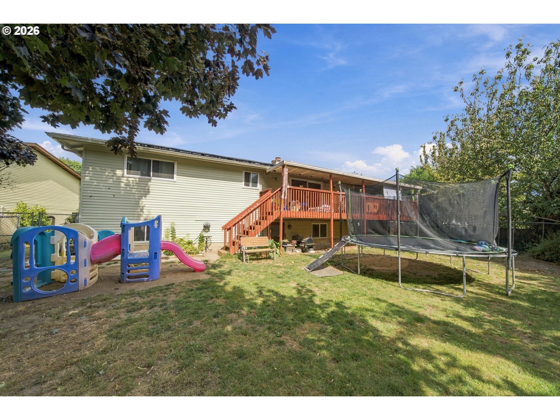 House backyard with raised wooden deck, children’s playset, and netted trampoline.