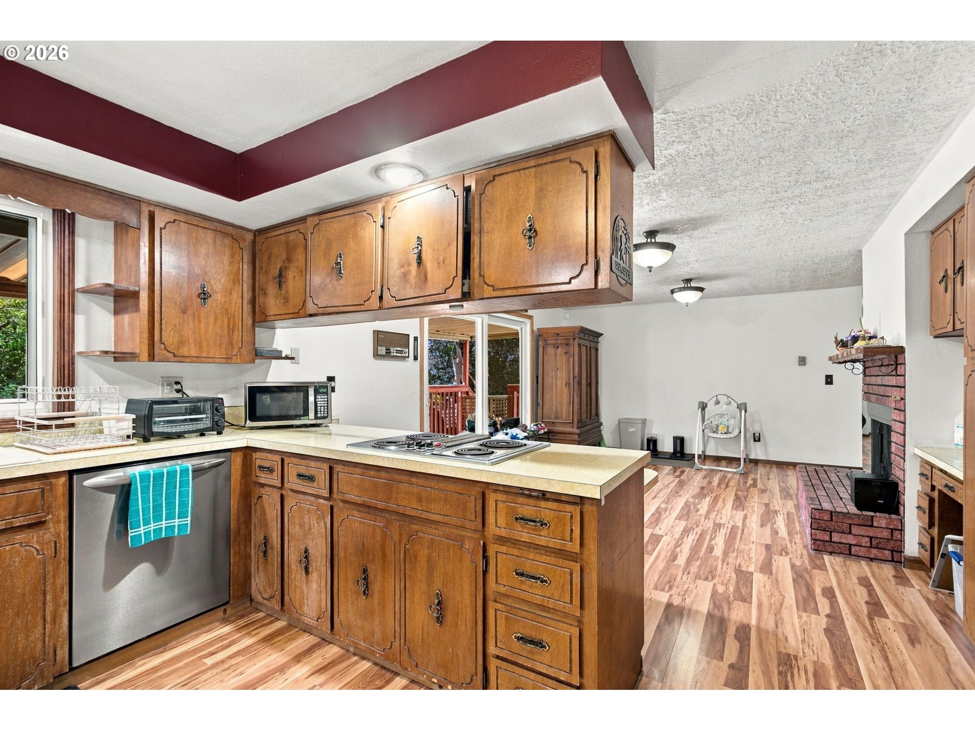 Kitchen with extensive wood cabinetry, a central cooktop island, and an adjoining living area with a brick fireplace.