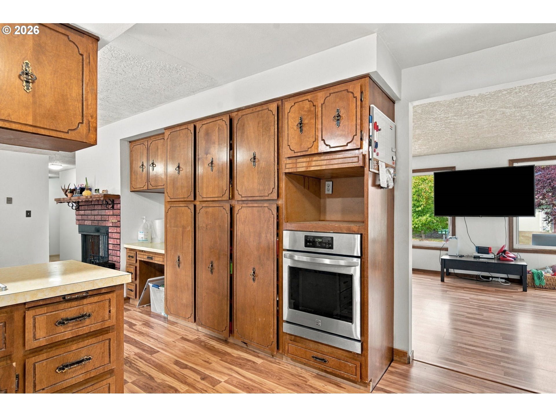 Kitchen with extensive wood cabinetry, a built-in stainless steel oven, and a brick fireplace nearby.