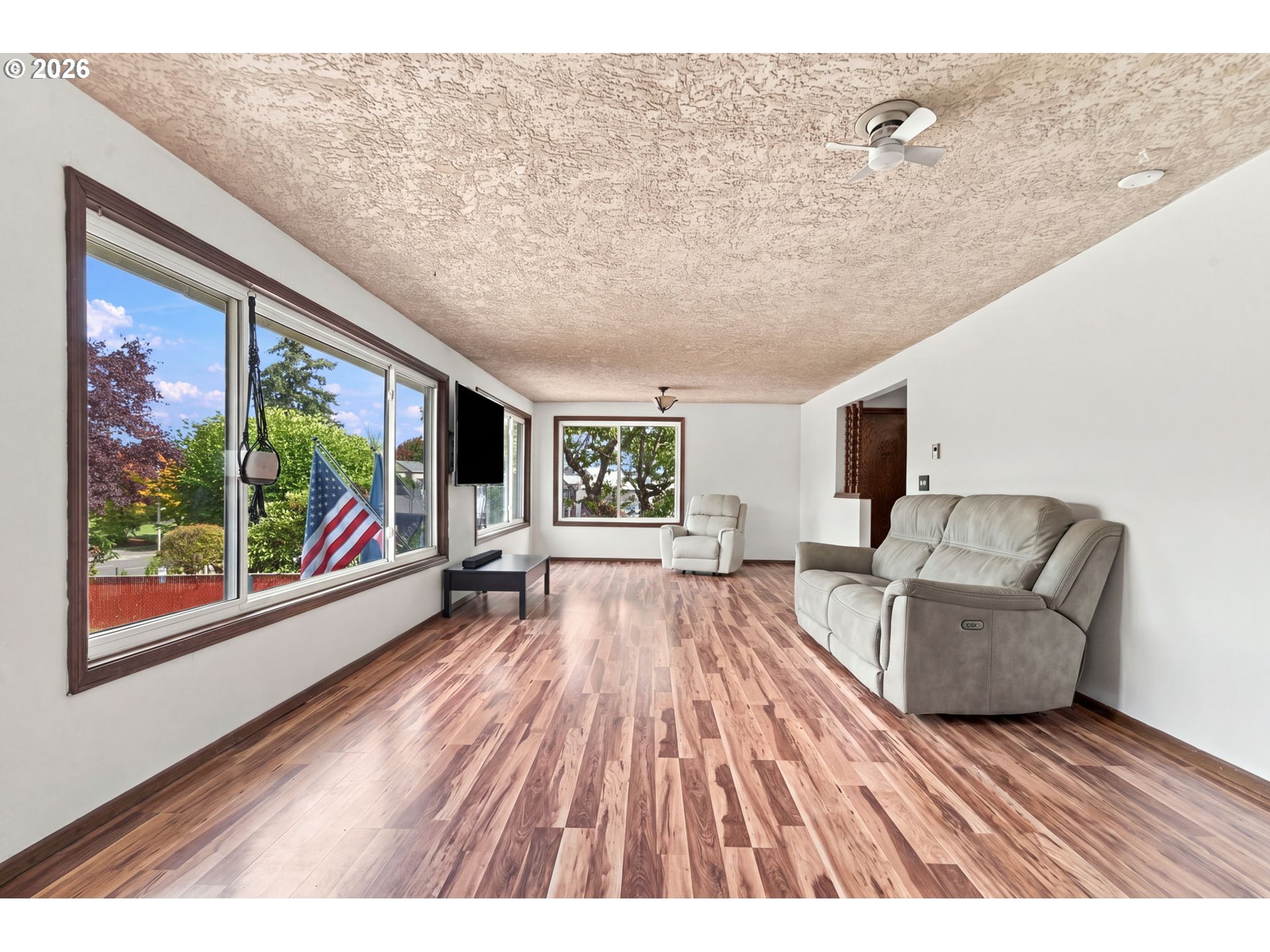 Living room with wood floors, large windows, a gray sofa, and an American flag.