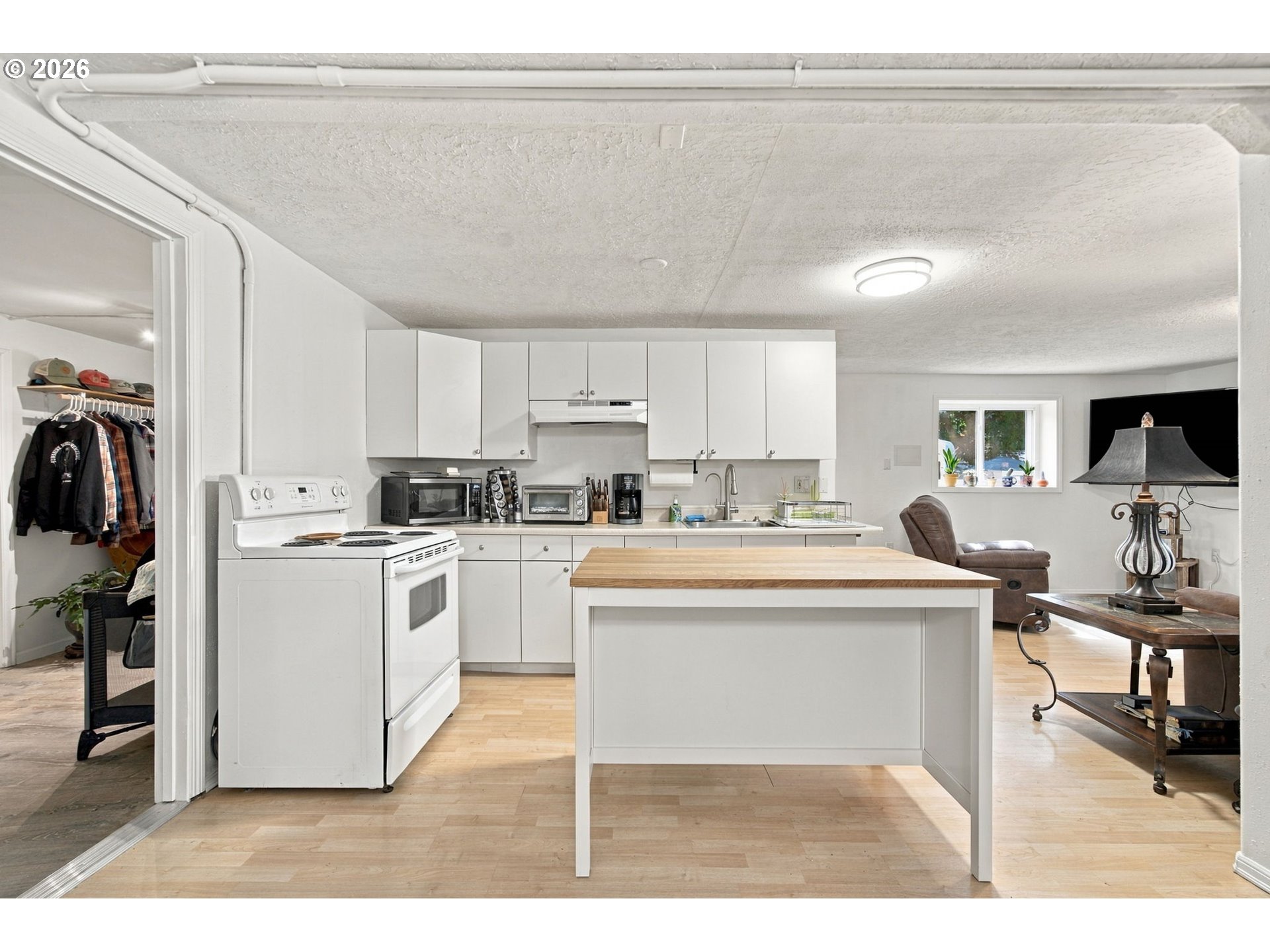 White kitchen with a wood-topped island opening into a living area with a brown recliner.