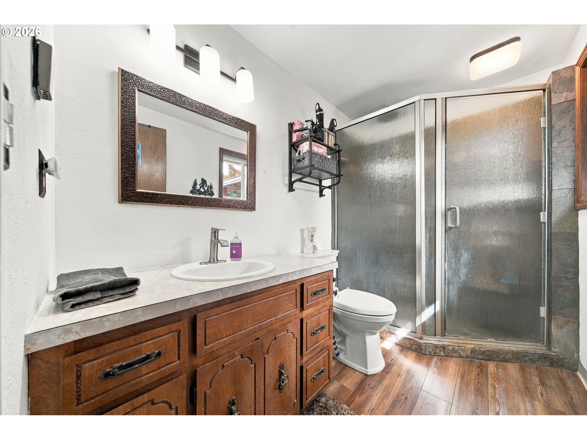Bathroom with a wood vanity, framed mirror, and frosted-glass shower enclosure.