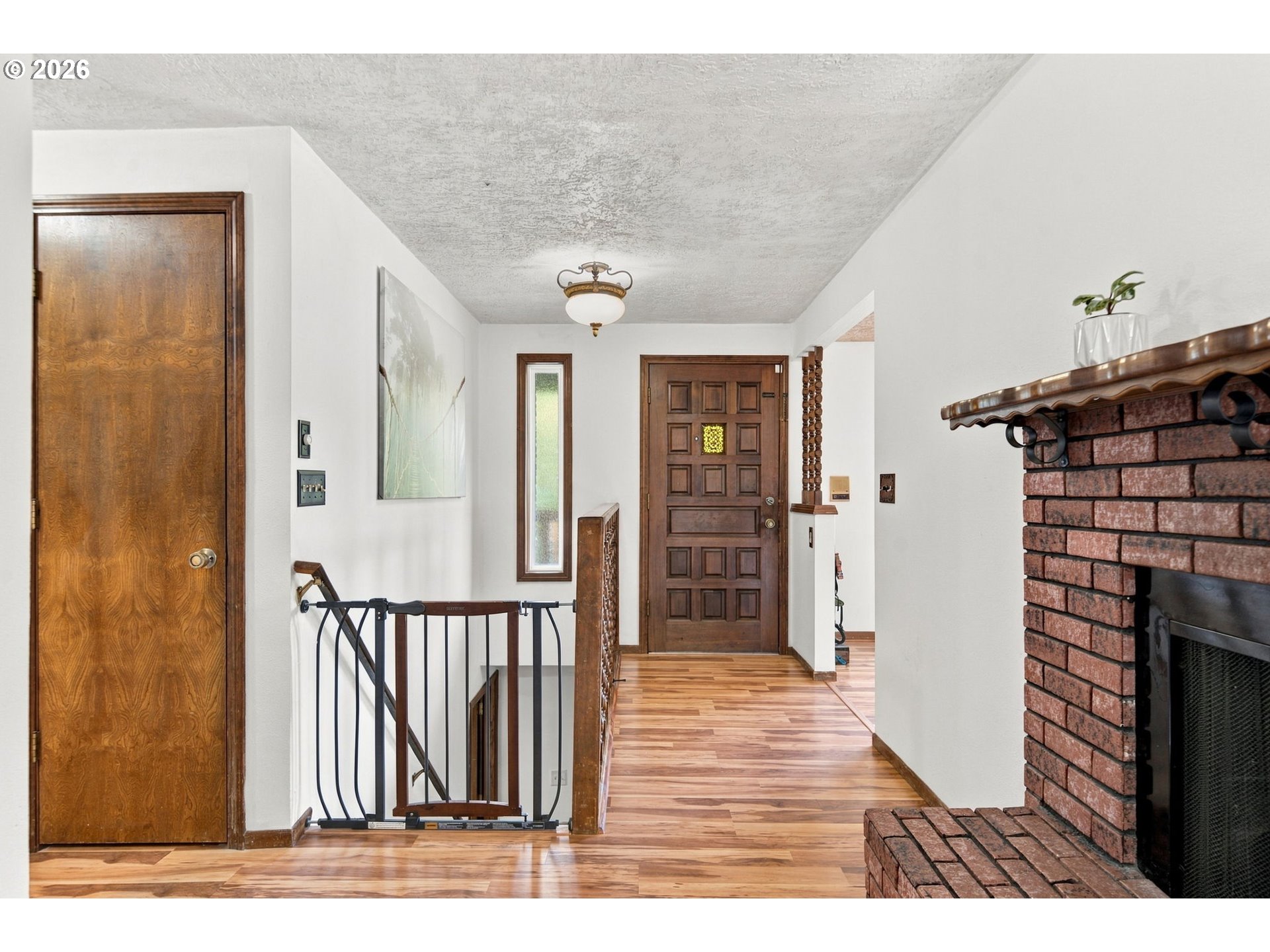 Entry hall with hardwood floors, a paneled wood front door, stair gate, and brick fireplace.