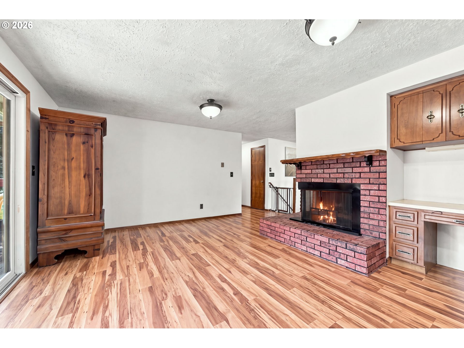 Living room with a brick fireplace, wood-look floors, built-in cabinets, and a sliding glass door.