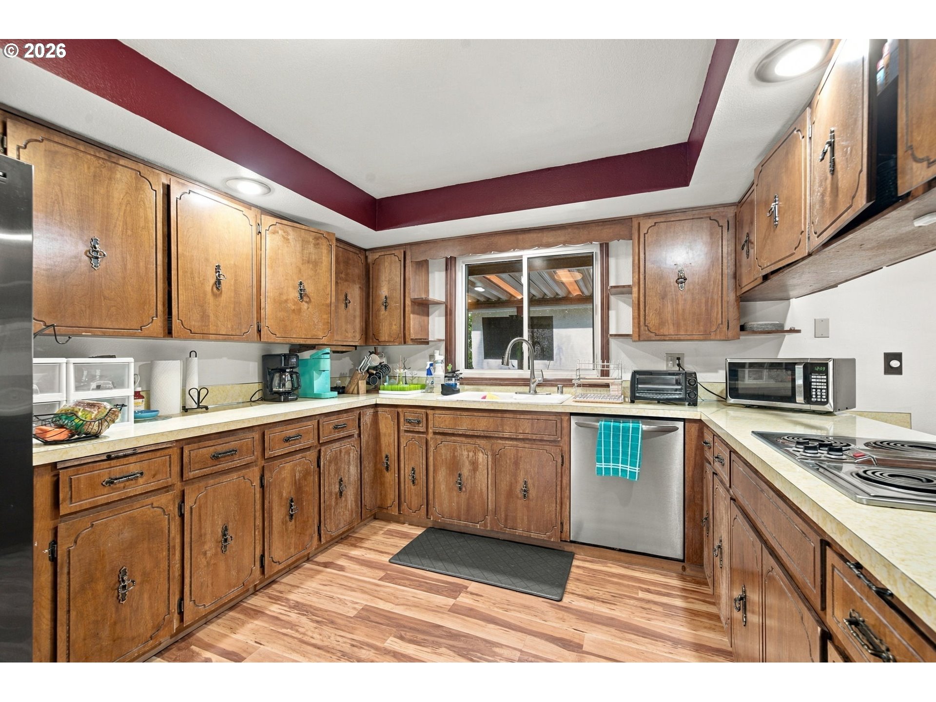 Kitchen with honey-brown wood cabinets, stainless steel appliances, and a burgundy tray ceiling.