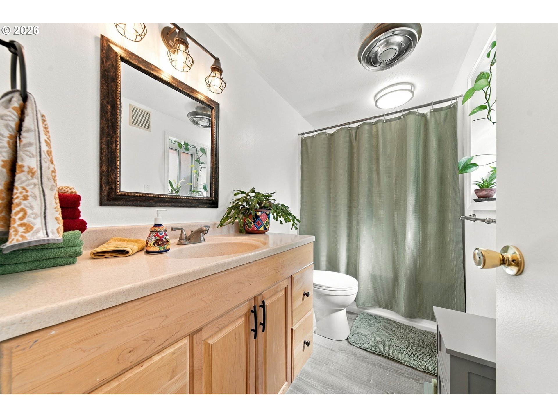 Bathroom with a light wood vanity, framed mirror, and green shower curtain.