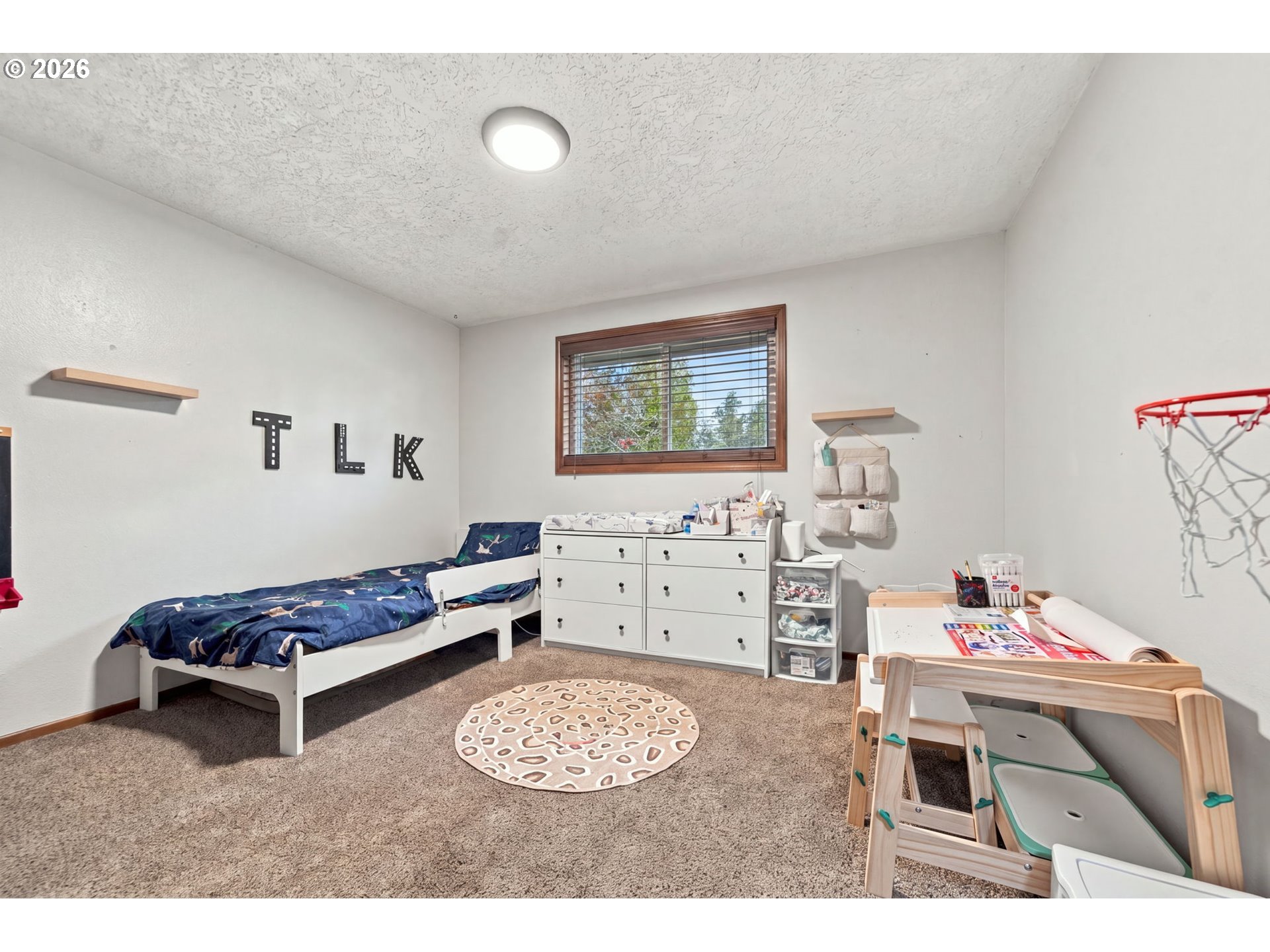 Child's bedroom with a single bed, white dressers, and a wooden activity table.