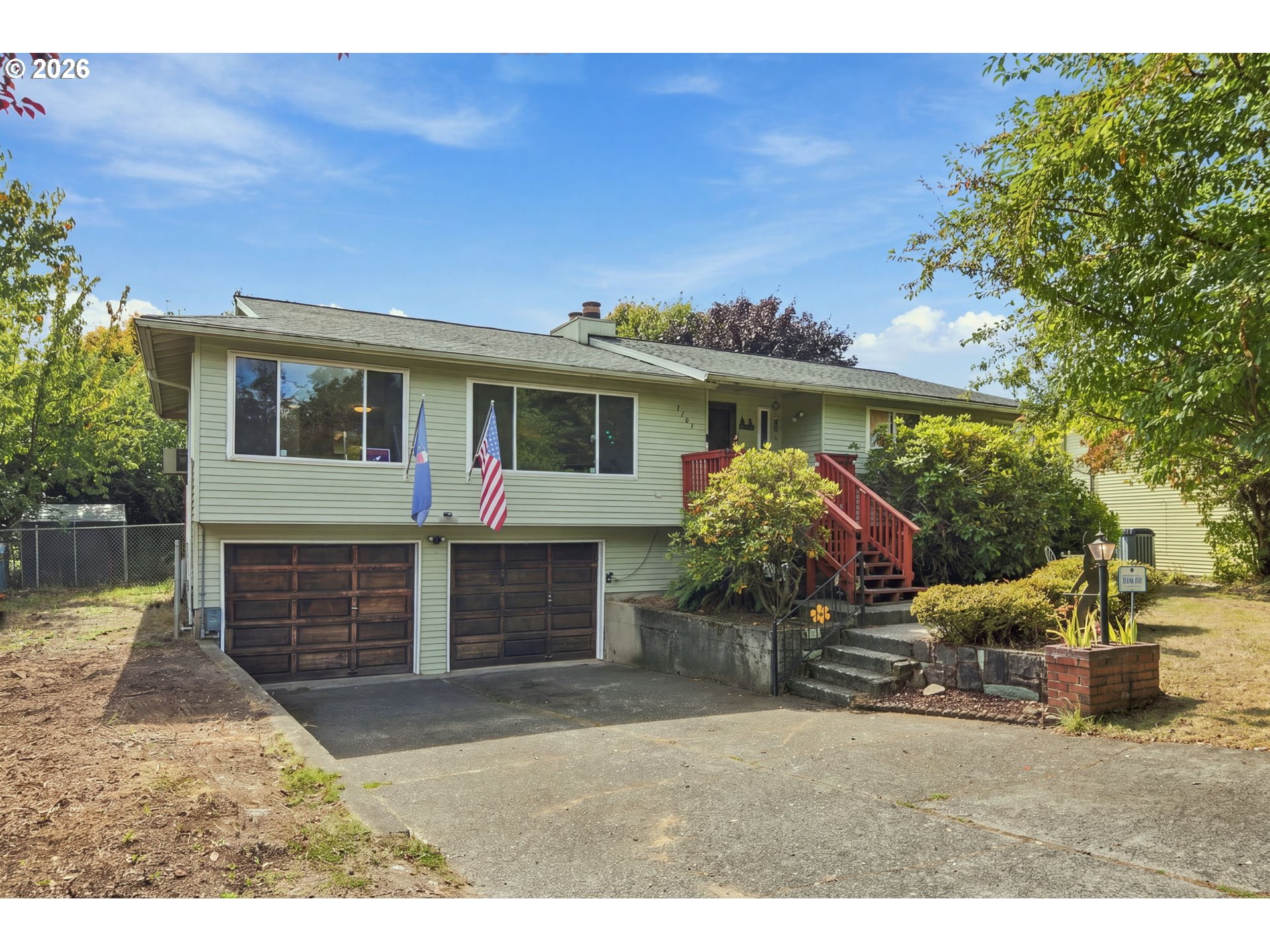 Pale green split-level house with two garage doors, red entry stairs, and flags by the driveway.
