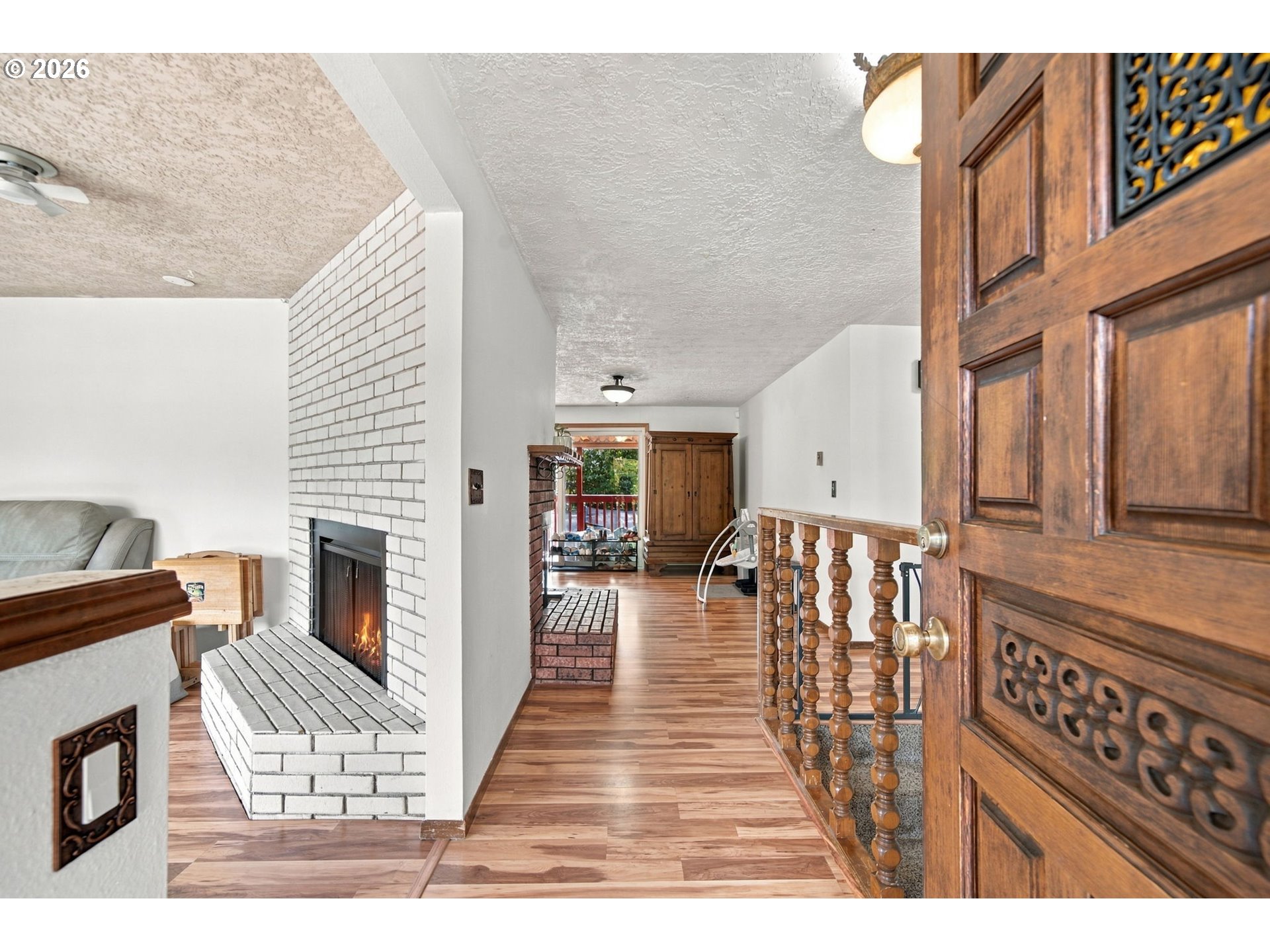 Entry hall with ornate wooden front door, wood floors, and a white brick fireplace.
