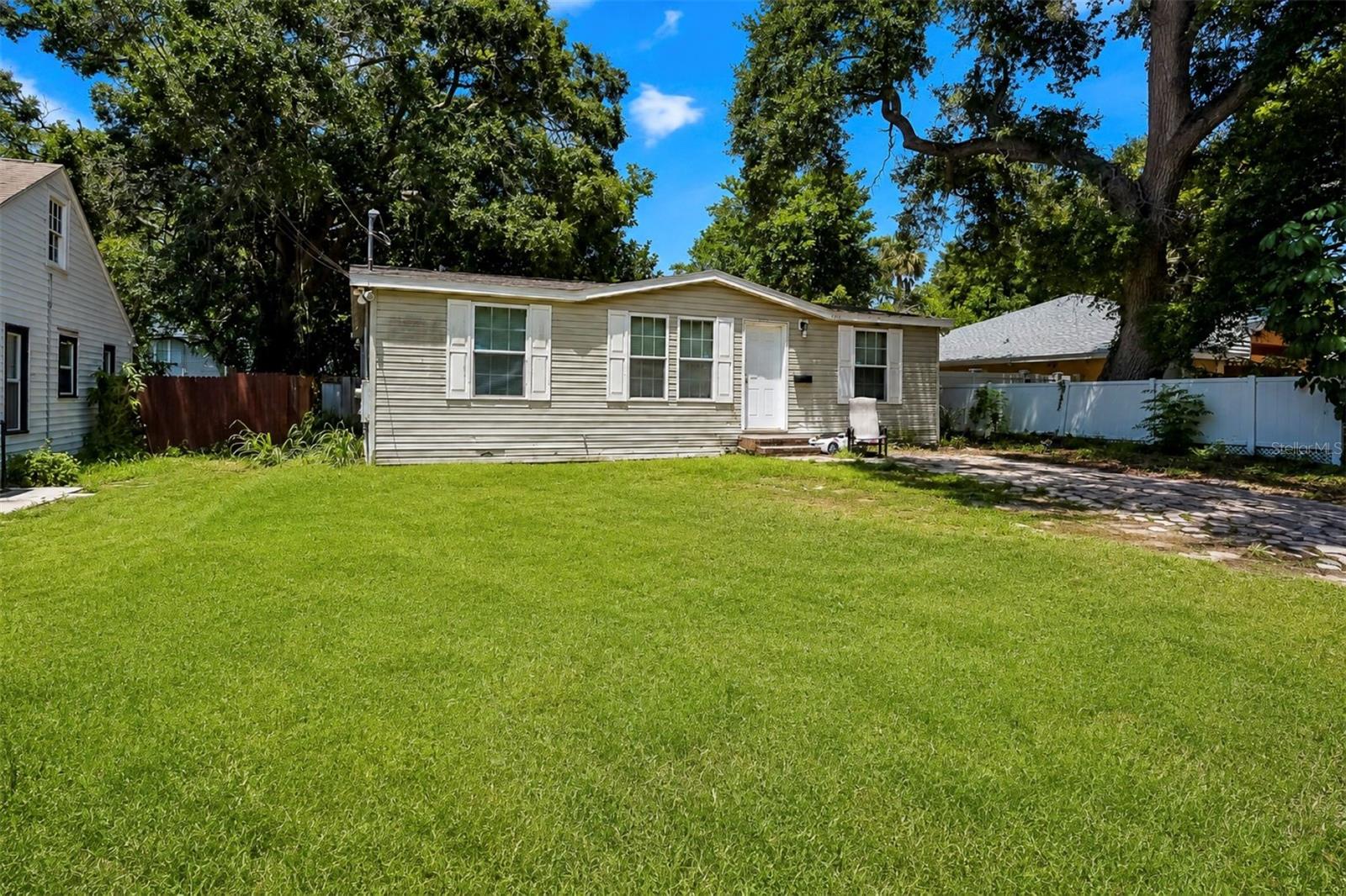 Single-story home with pale siding, a broad green lawn, and mature shade trees.