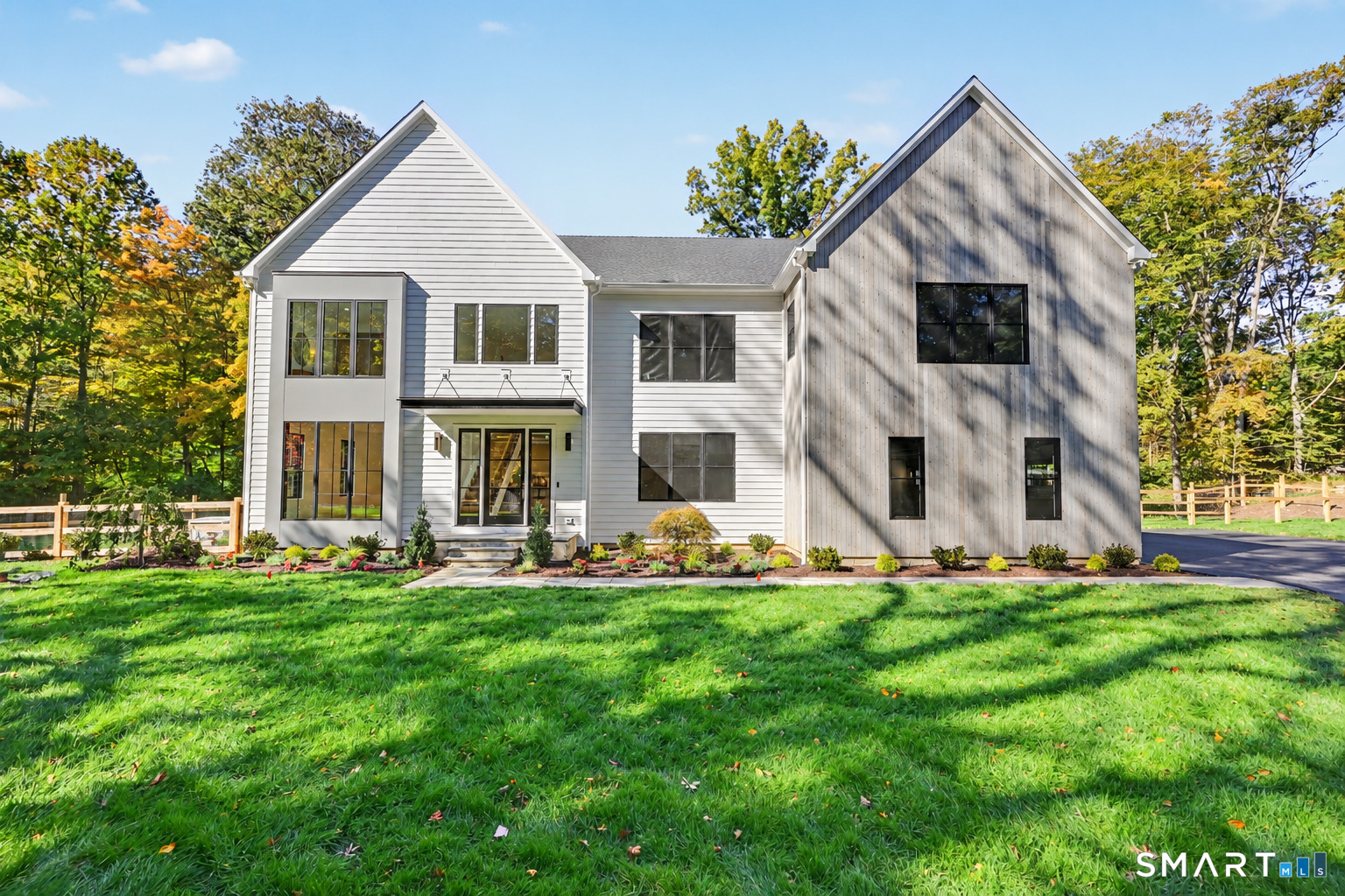 Modern two-story home with white and wood siding, black-framed windows, and a landscaped lawn.