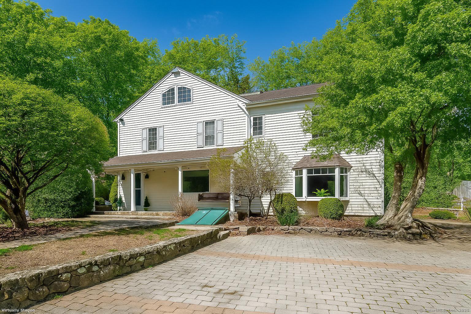 White two-story house with a covered entry and bay window, framed by mature trees.
